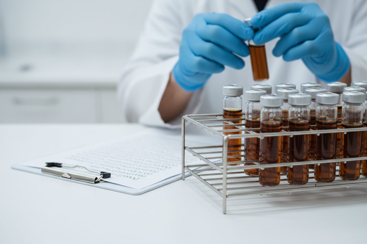 Lab vial rack and clipboard with gloved hands inspecting a sample